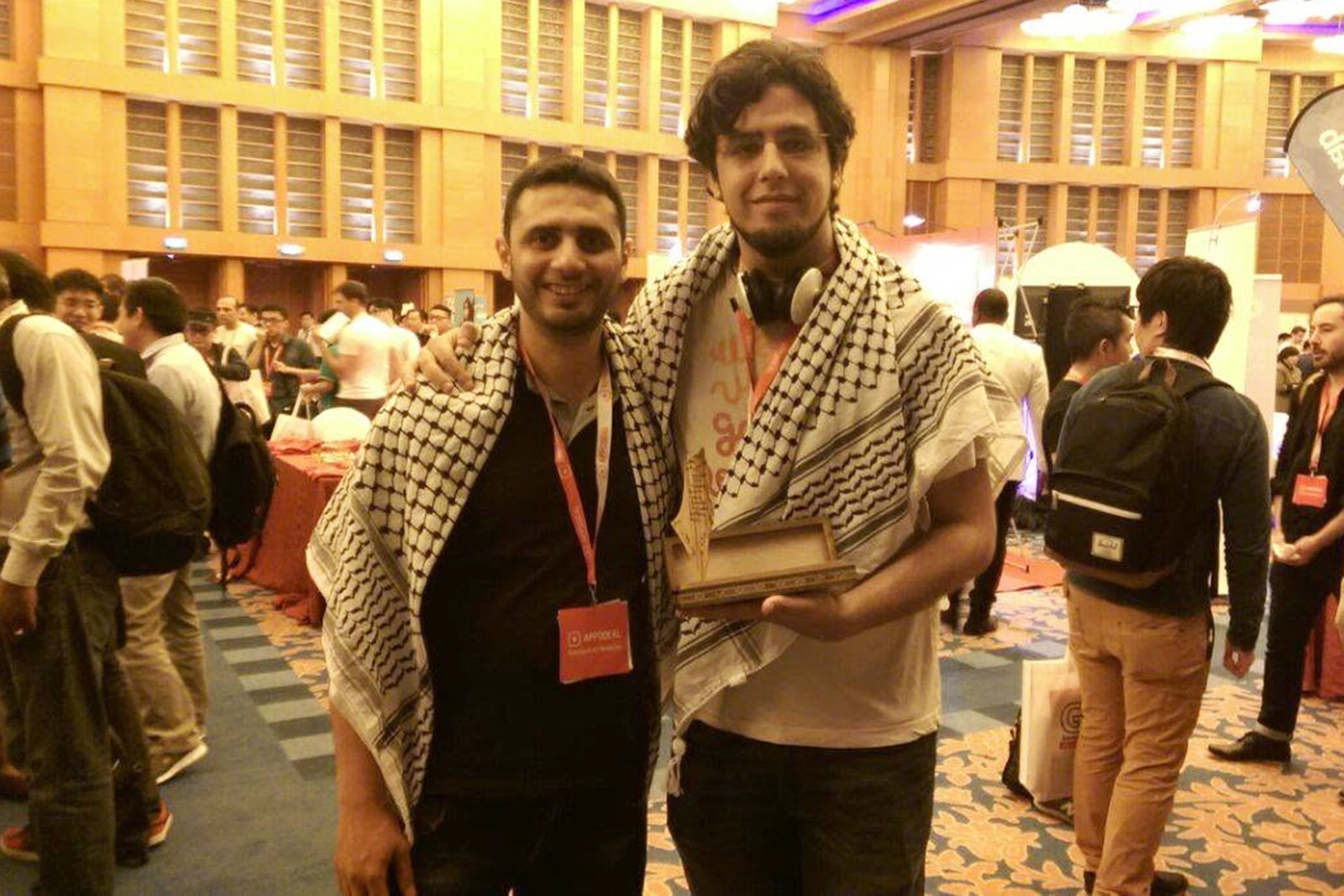 A photograph of Rami Ismail with his arm round Palestinian developer Rasheed Abueideh (who is to his left), the first time they met at a gaming event in Singapore in 2016. Both men are wearing keffiyehs