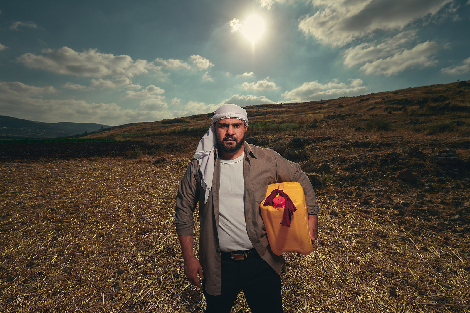 A promotional photograph for Alaa Shehada and Sam Beale's play The Bridge, featuring Shehada as the main character, carrying a container of olive oil across countryside