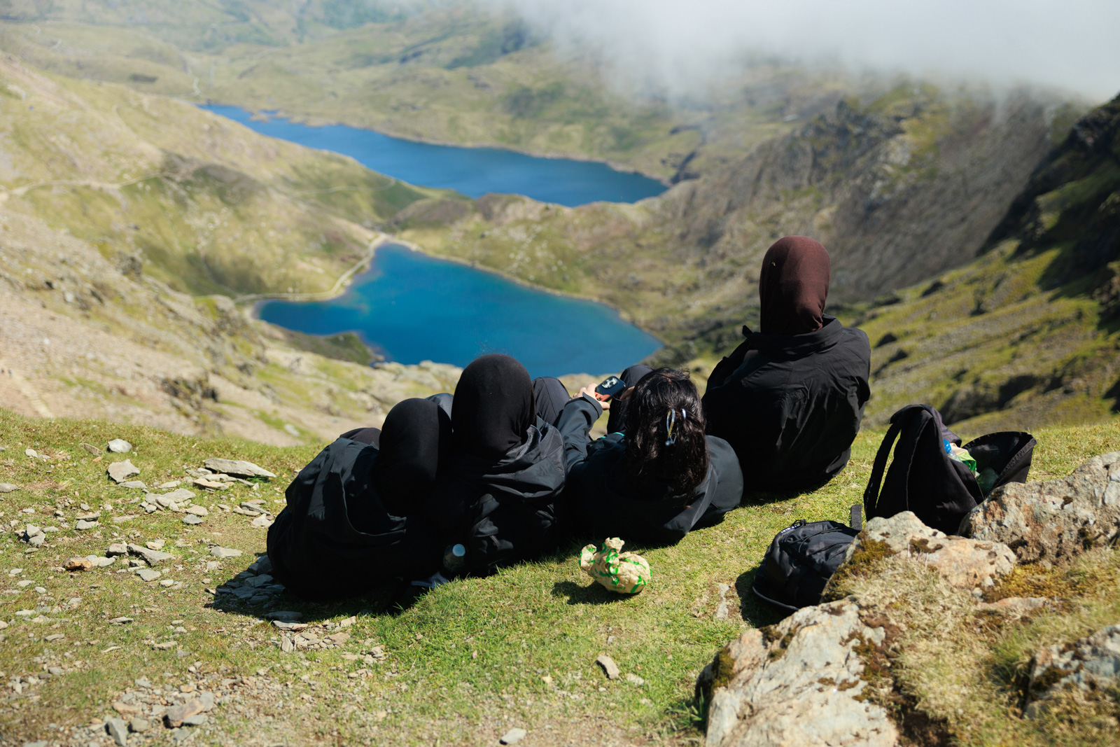 A photograph of a group of walkers sitting down and taking a break overlooking two lakes during a Human Appeal Snowdonia trek