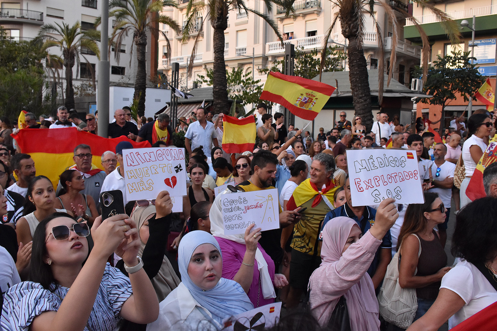 A diverse crowd hold hand-drawn signs and mobile phones aloft