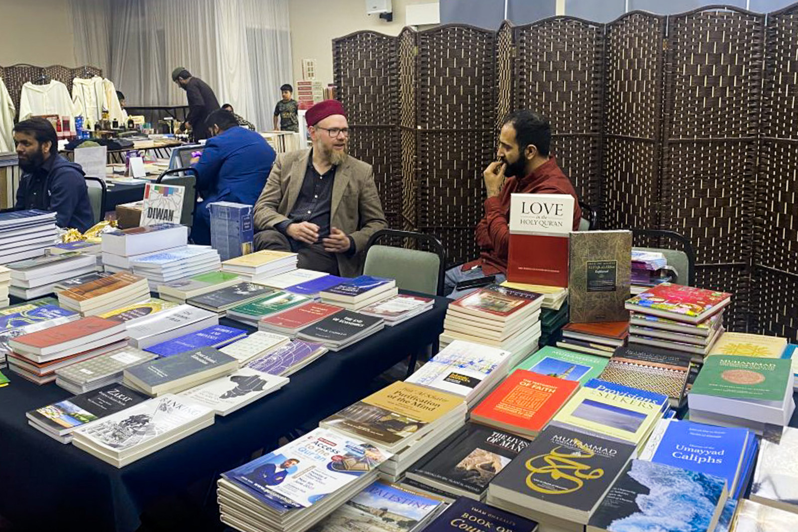 A photograph of a Muslim Lit Fest book bazaar, with two stallholders chatting in the foreground