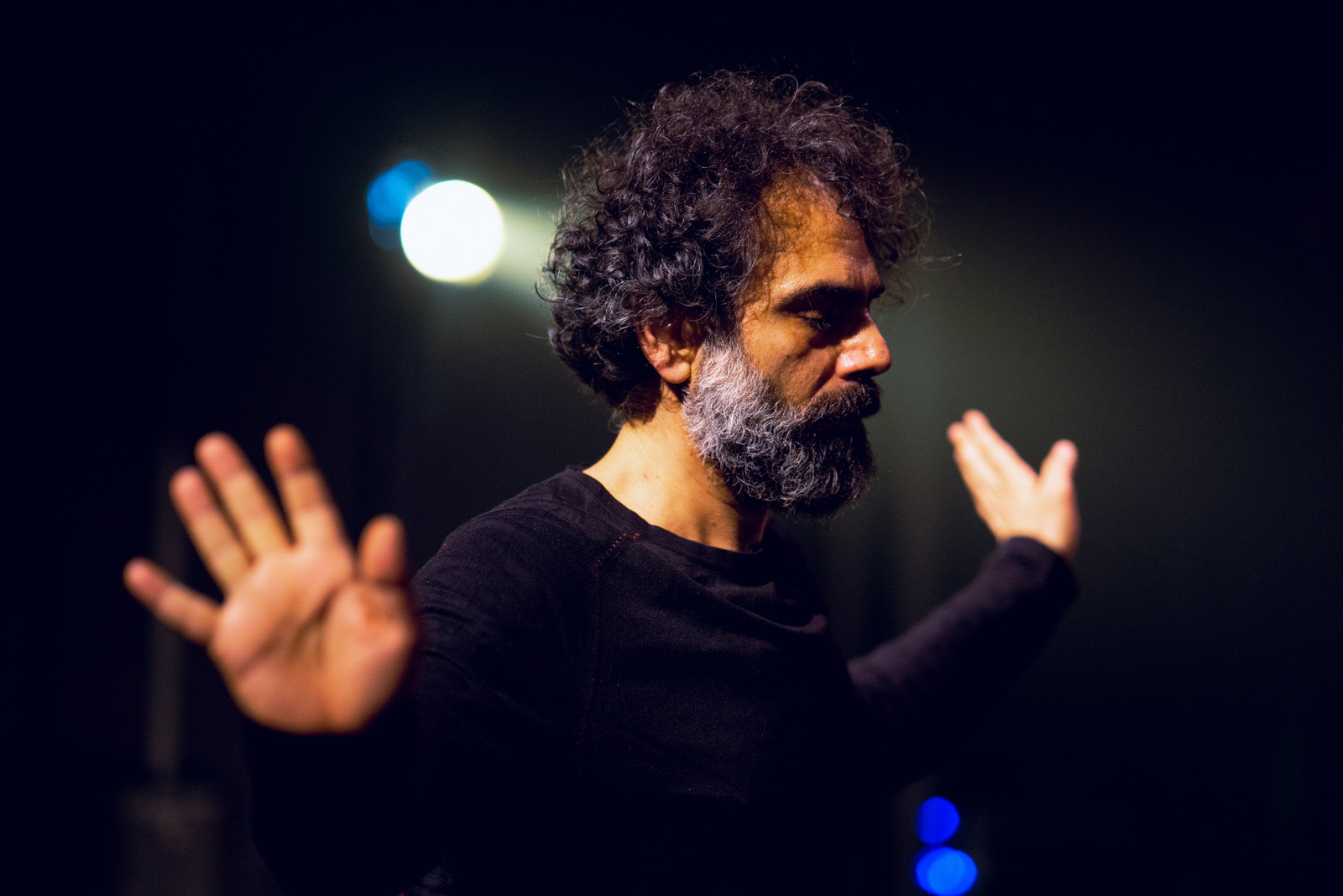 A close-up head and shoulders photograph of a dancer Omar Rajeh performing, standing with eyes closed and hands outstretched at shoulder height