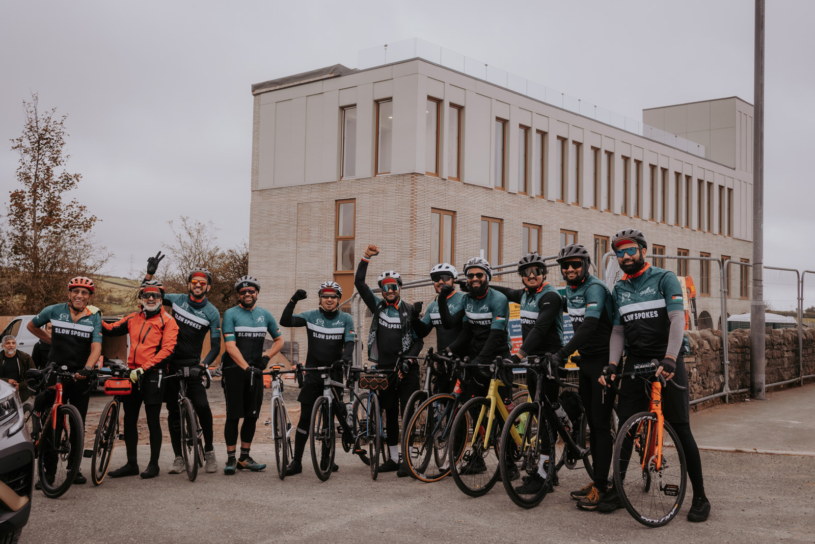 A photograph of members of Slow Spokes cycling club — in riding gear and on their bikes — outside the South Lakes Islamic Centre, Dalton-in-Furness