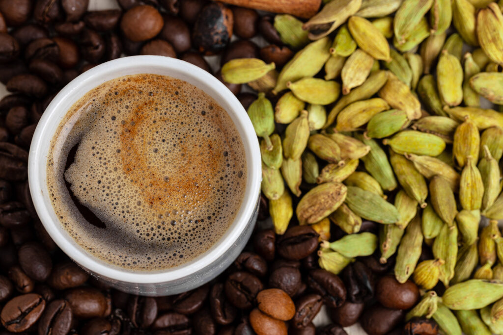 Stock photograph of a cup of coffee with roasted beans, cardamom and cinnamon close up