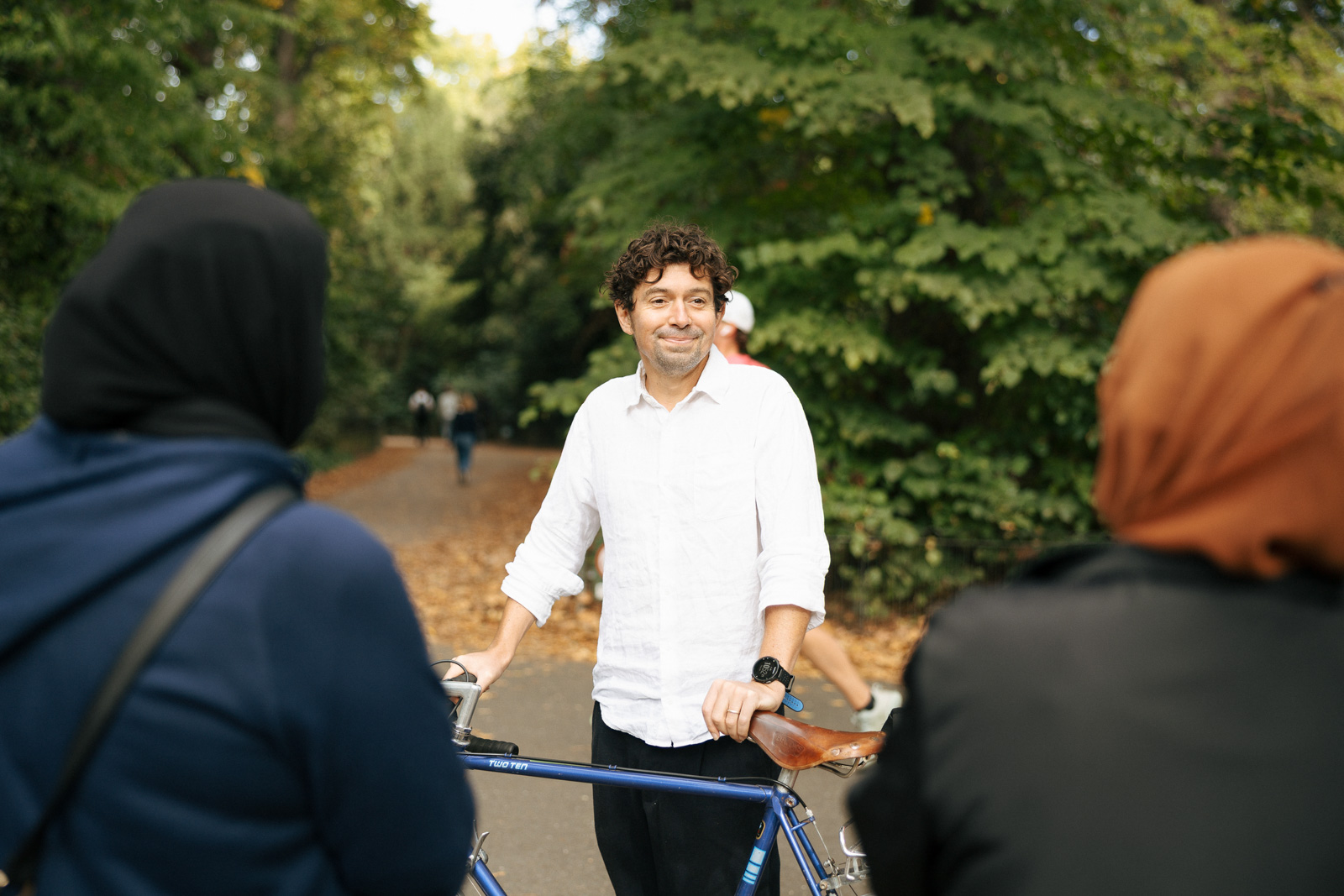 A photograph of Dermot Bryers leaning against his bike in Battersea Park, smiling as he speaks to ESOL learners during an English for Action walk and talk session