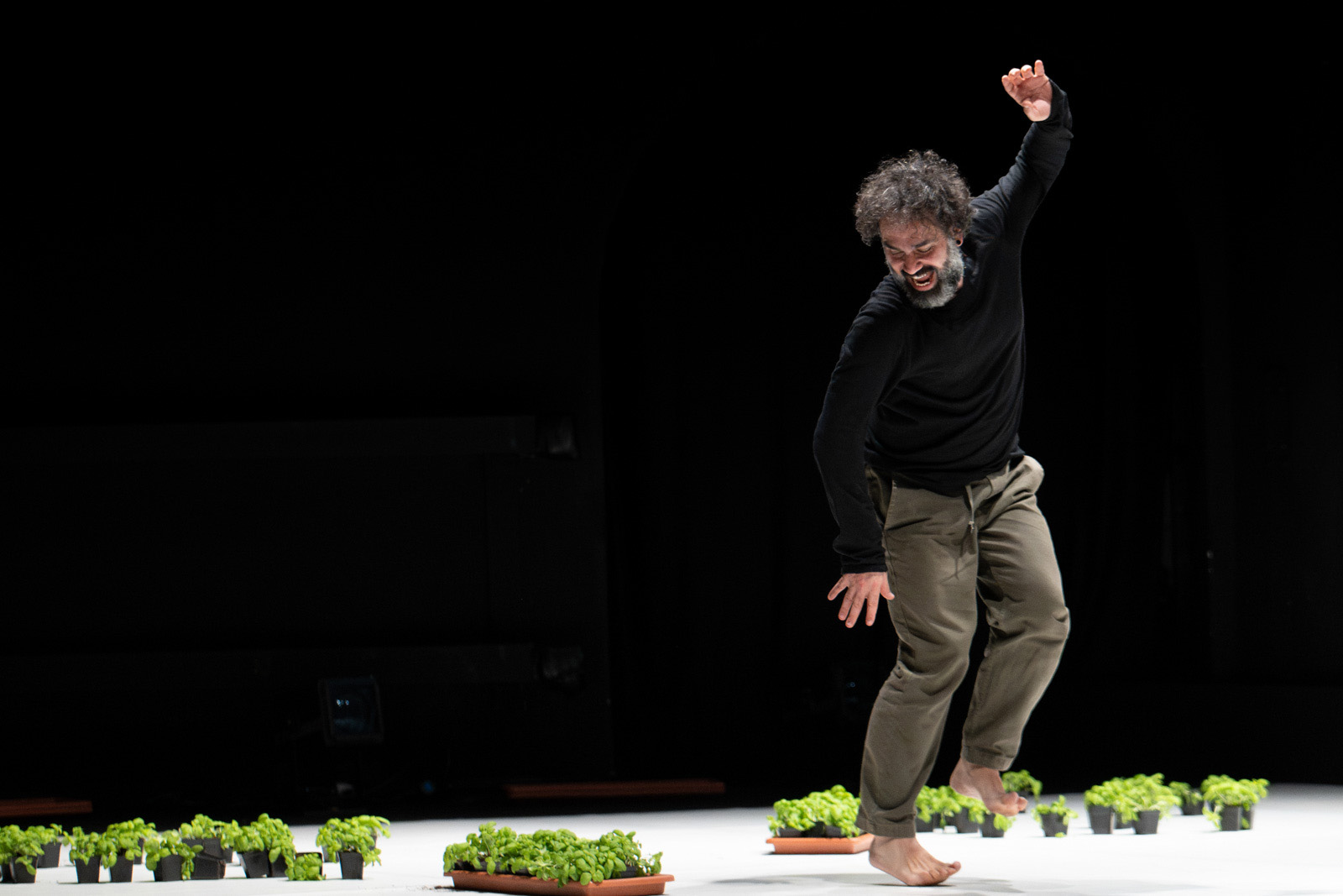 Omar Rajeh performing his latest work, Dance is Not for Us, bare foot and balancing on the ball of his right foot, wearing a black top and green trousers