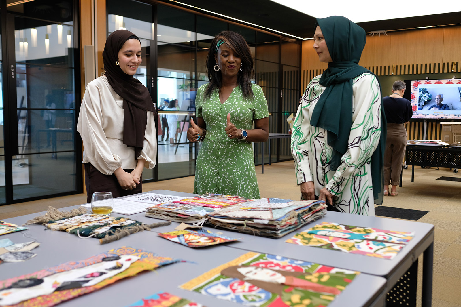 Three women stand smiling and talking at a table filled with artwork