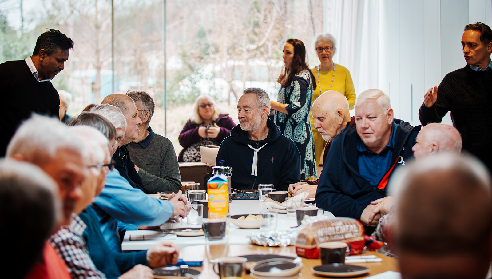 A group of men and women chatting around a table with coffee cups and glasses.