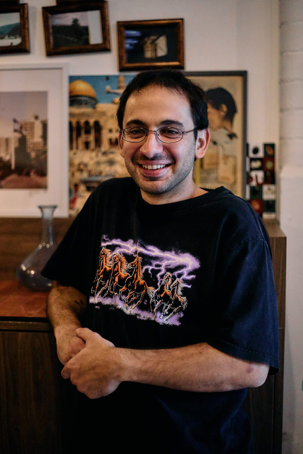 A portrait photograph of Edami co-founder Minas Missirian, who is seated, wearing a T-shirt and smiling, in the bakery