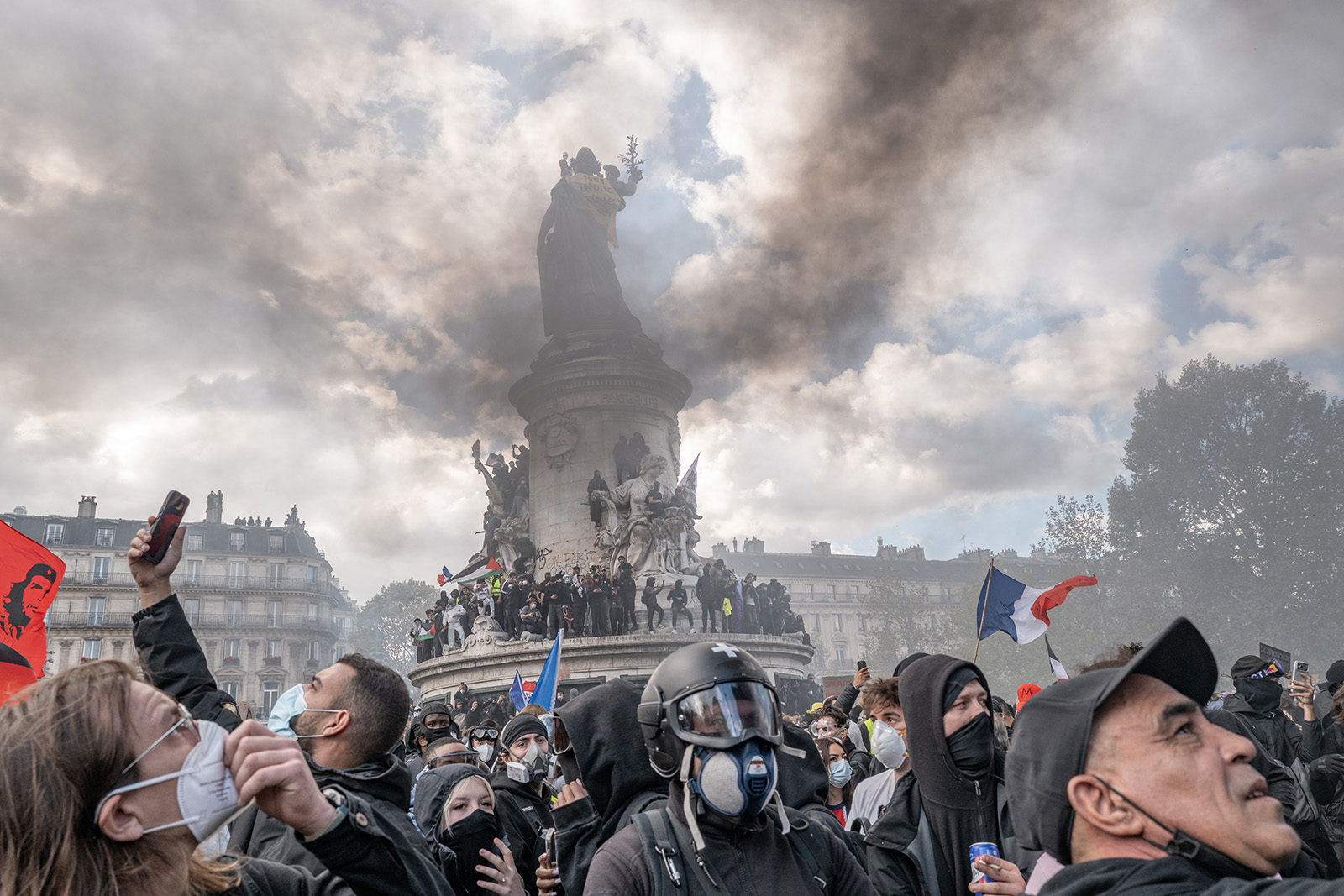 Smoke billows as people stand on the plinth of the Statue de la République, seen from behind