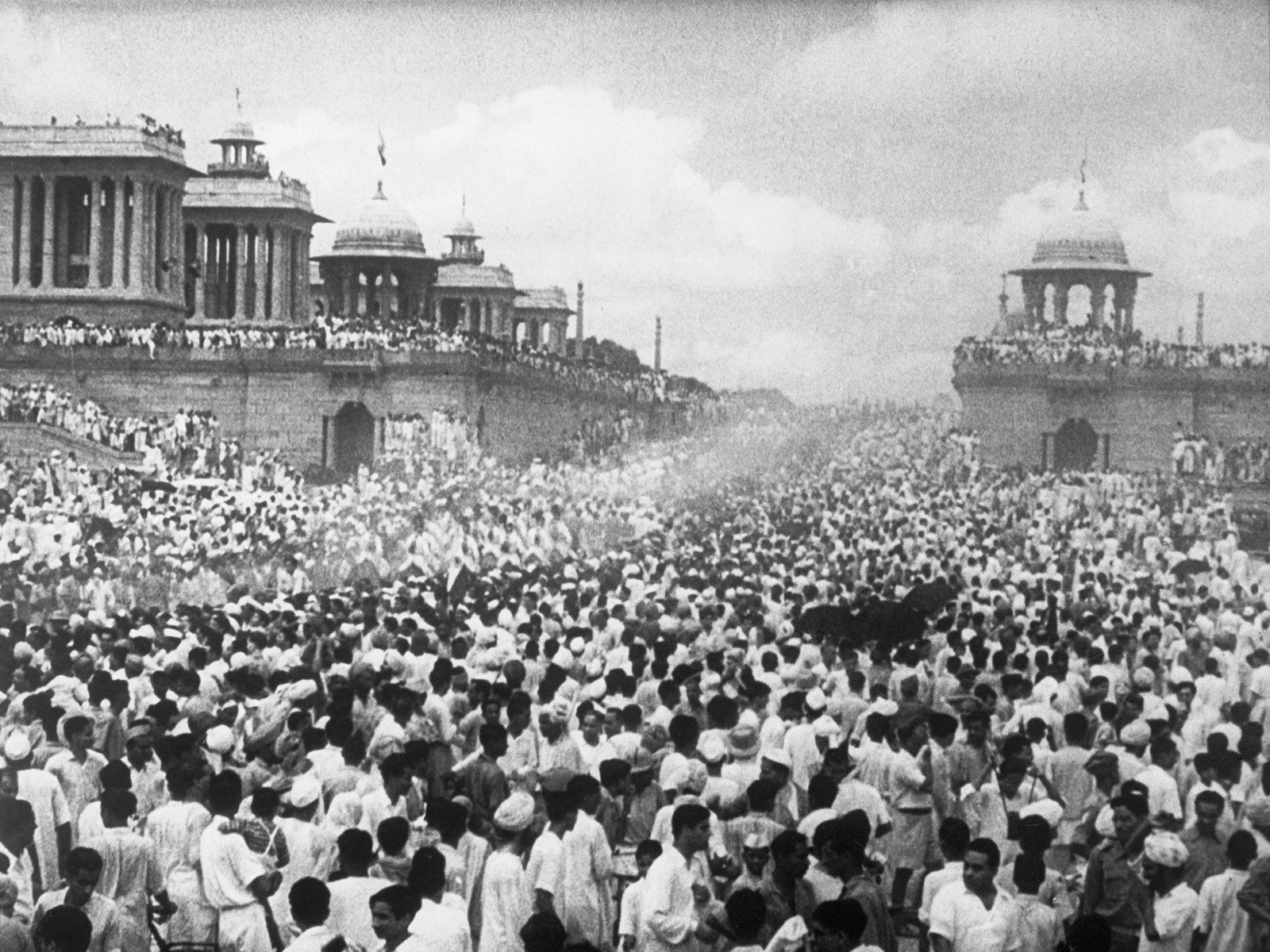 A black and white image of a huge crowd filling the street outside a grand building with pillars and domes