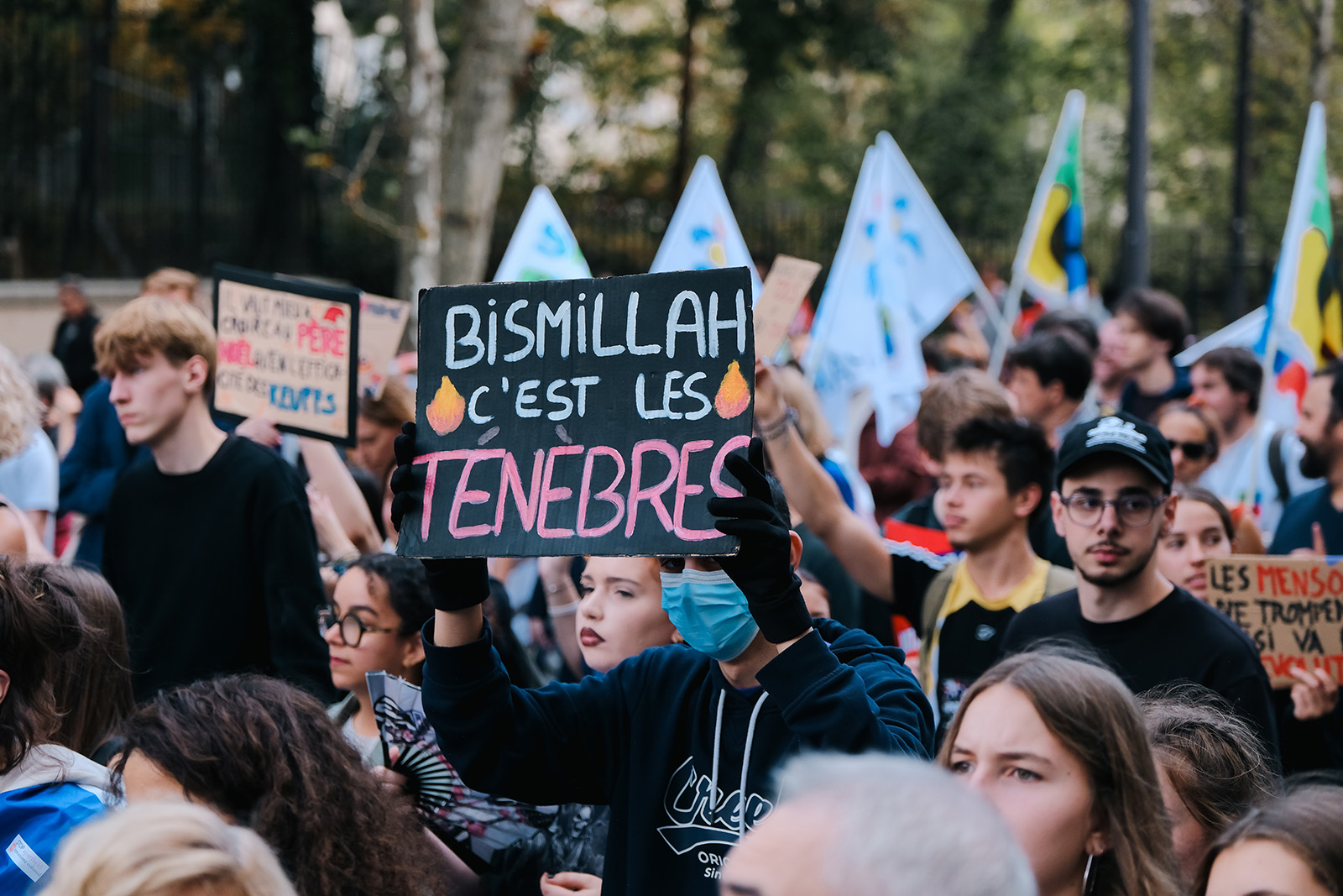 A crowd of young people with serious faces, one holding the sign described in the caption