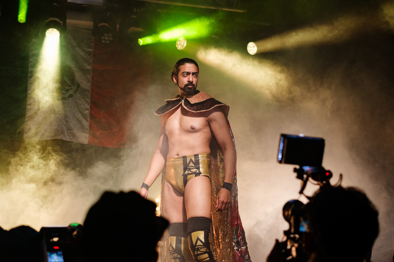 A photograph of Malik Waseem, whose Lucha Britannia character is based on the Mesopotamian god Marduk, making a dramatic entrance in a gold cape and shorts surrounded by dry ice for the bout at the Garage, 17 September 2026